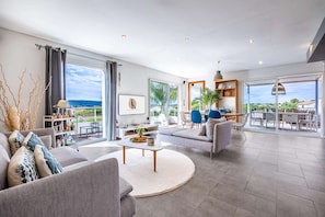 A spacious living area with a large window, a sofa, a coffee table, and a dining area with chairs. - Villa, heated pool, exceptional view, exotic garden, 4-star rating (Montbazin)