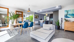 A modern living room with a sofa, dining area with chairs, a kitchen, and a large window. - Villa, heated pool, exceptional view, exotic garden, 4-star rating (Montbazin)