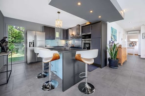 A modern kitchen with a central island, bar stools, and a view of the outdoors. - Villa, heated pool, exceptional view, exotic garden, 4-star rating (Montbazin)