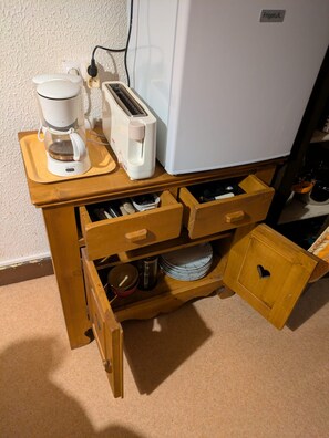 A kitchenette with a coffee maker, toaster, and a small refrigerator. There are wooden drawers and a cabinet with various kitchen items. - Apartment in the center of the village of Combloux (Combloux)