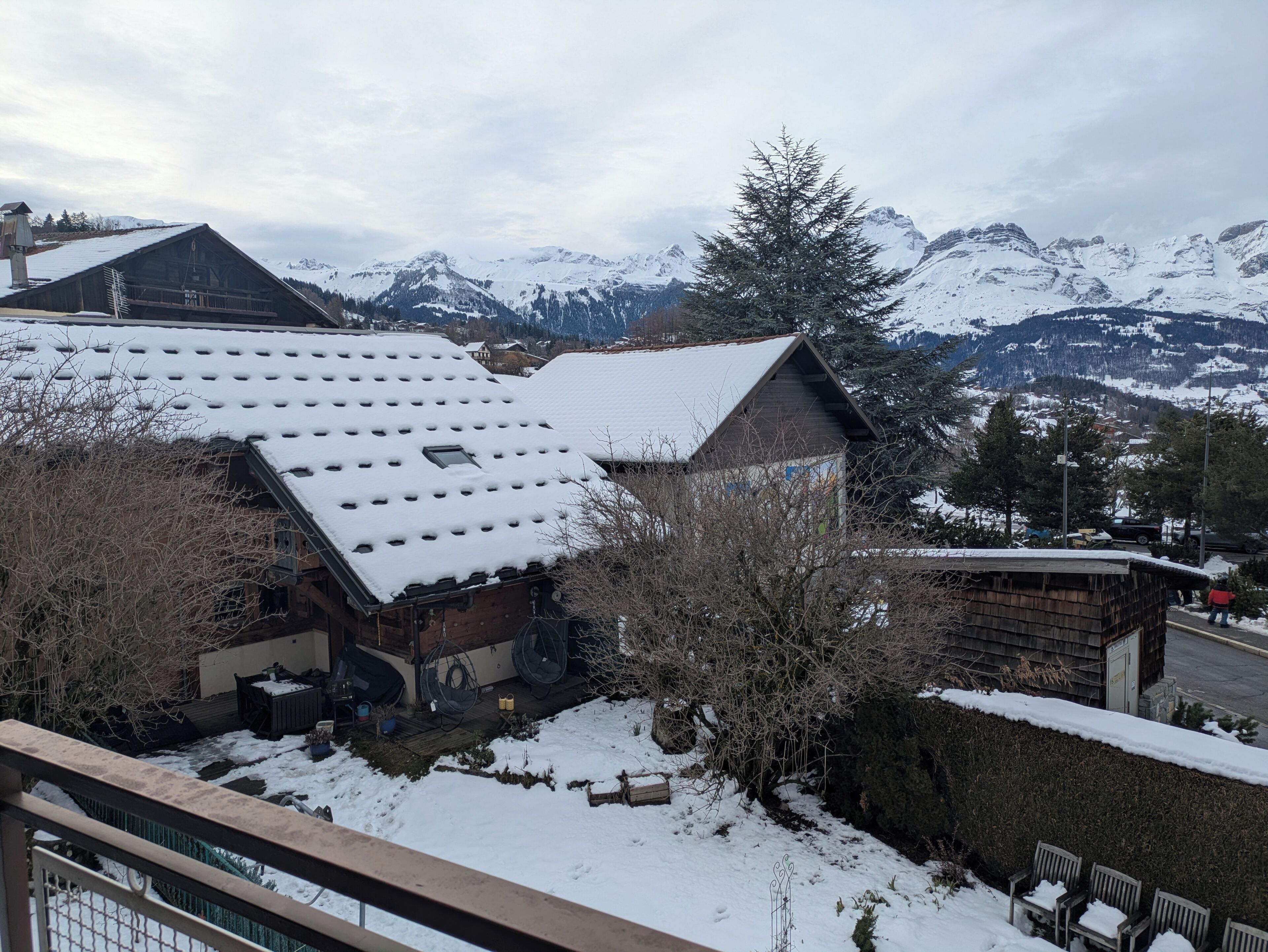 Ein schneebedecktes Gebäude mit geneigtem Dach, umgeben von schneebedeckten Bäumen und Bergen im Hintergrund.