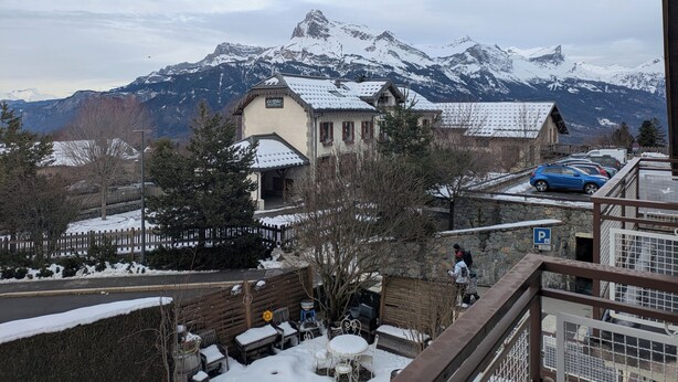 A mountain resort with snow-covered roofs, a parking area, and a view of snow-capped peaks. - Apartment in the center of the village of Combloux (Combloux)
