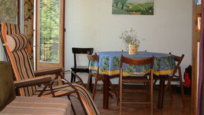A dining area with a table set for four, chairs, a window with a view of greenery, and a painting on the wall. - Apartment in the center of the village of Combloux (Combloux)