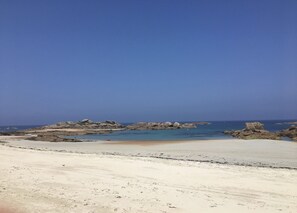 A beach with clear skies, rocky outcrops, and calm waters.
