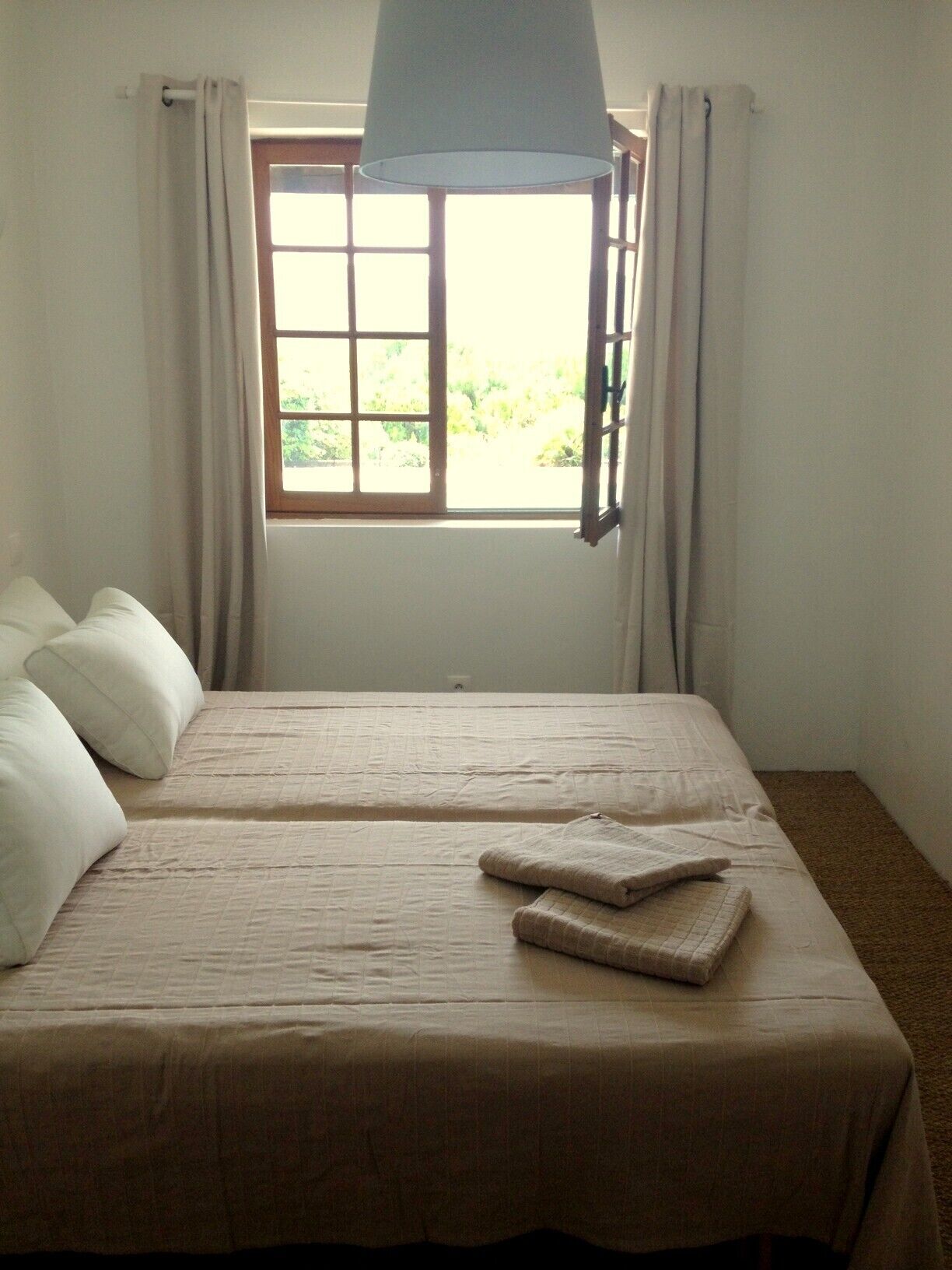 A bedroom with a bed, curtains, a window, and a view of greenery outside.
