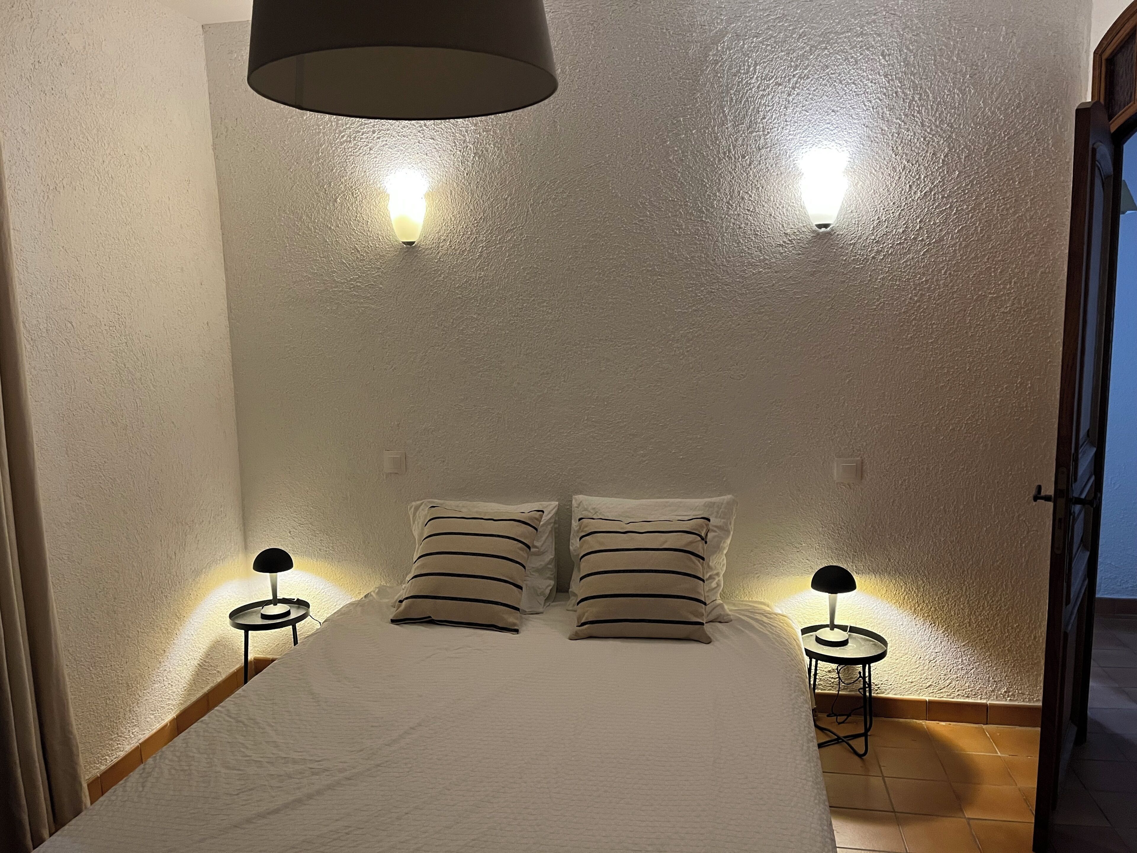 A bedroom with a bed, two bedside tables, two wall-mounted lamps, and a door.