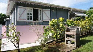 Una casa a un piano con facciata rosa, un piccolo portico e una griglia per barbecue in cemento.