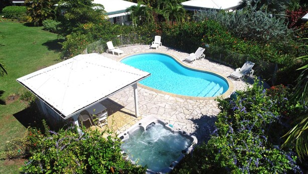 Una piscina con lettini, una vasca idromassaggio e una veranda coperta immersa nel verde.