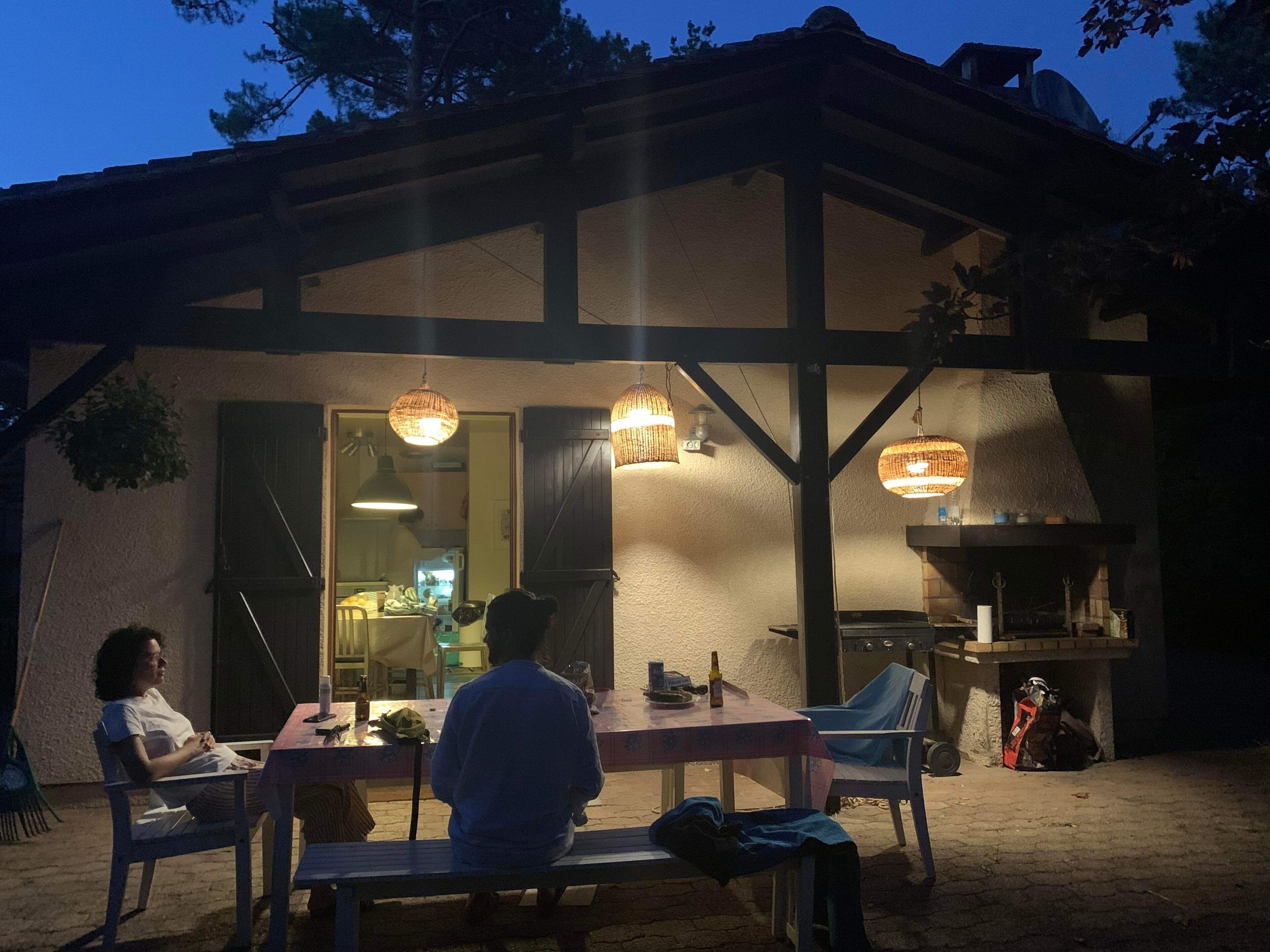 Ein Außenbereich mit einer Holzpergola, einem Grill und hängenden Lichtern.