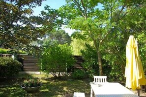 A garden with a white table and yellow umbrella, surrounded by lush greenery and a wooden staircase.