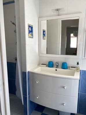 A bathroom with a white sink, blue tiles, a mirror, and a shower area.
