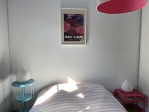 A bedroom with a bed, a framed movie poster on the wall, a blue side table, and a pink side table.