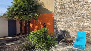 A courtyard with a palm tree, a stone wall, and a blue chair. - Fully renovated house, all comforts, near beach, free wi-fi access.  (La Bernerie-En-Retz)