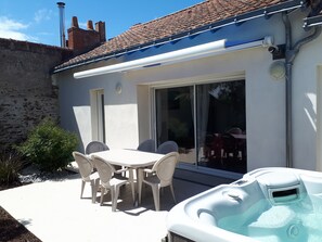 Une terrasse avec une table et des chaises, un jacuzzi et une porte vitrée donnant sur un espace abrité.