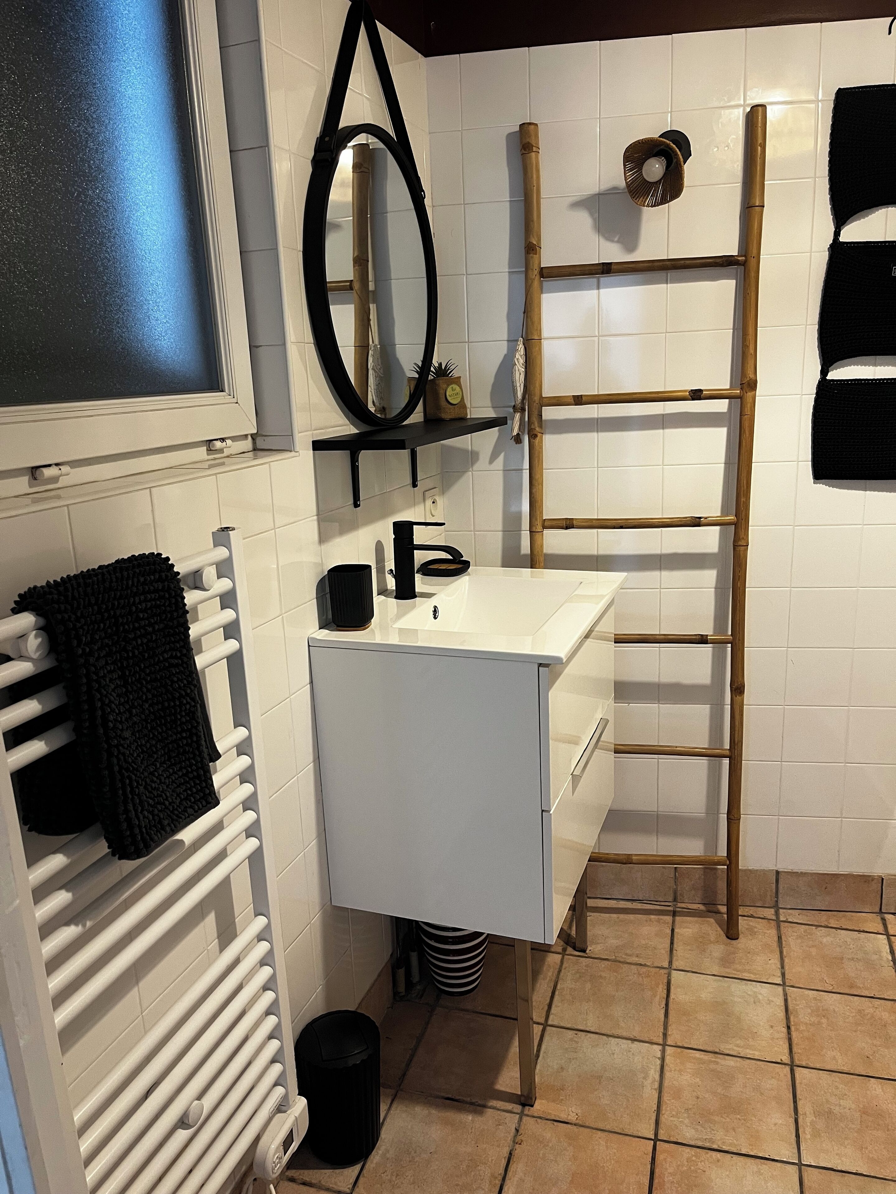 A bathroom with a white sink, black towel, and a bamboo ladder.