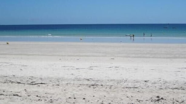 Een strand met een heldere lucht en een kalme zee.