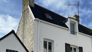 Een wit gebouw met zwarte luiken, het nummer '29' op de deur en een klein raam met gordijn.