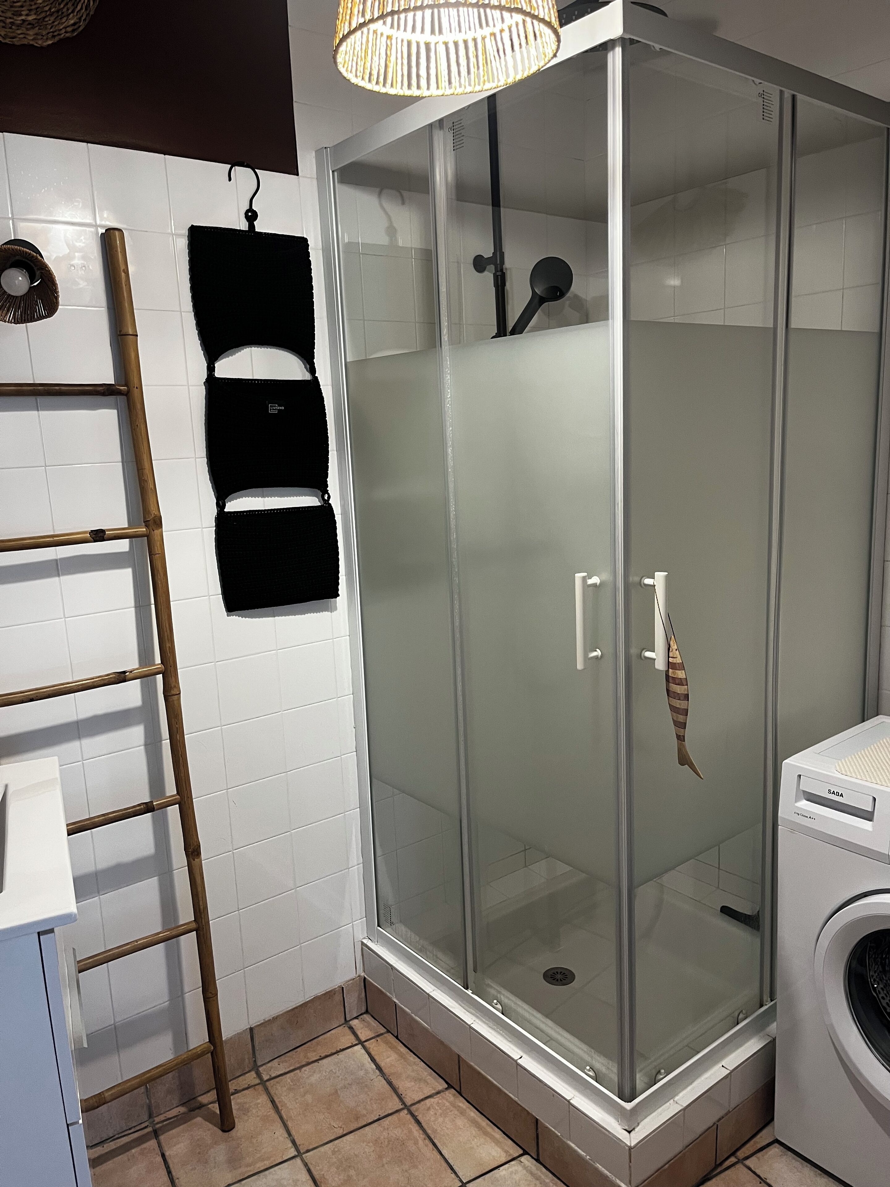 A modern bathroom with a glass-enclosed shower, a bamboo ladder, a black towel, and a white washing machine.