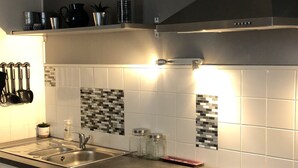 Een moderne keuken met witte kastjes, een RVS vaatwasser, een zwart aanrecht en een betegelde achterwand met een mozaïekpatroon.