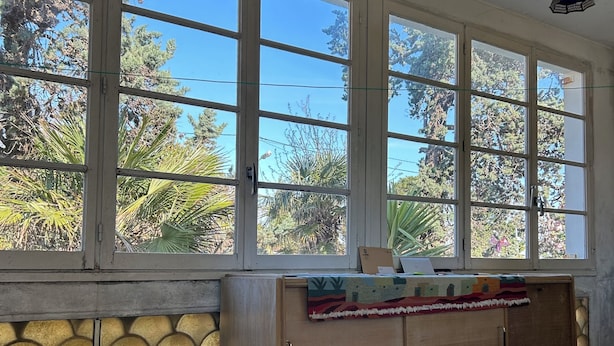 A room with large windows, a wooden cabinet, a bench, and a patterned rug.