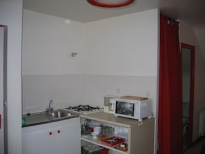 Une petite cuisine avec des meubles blancs, une cuisinière à gaz, un four à micro-ondes et un évier.
