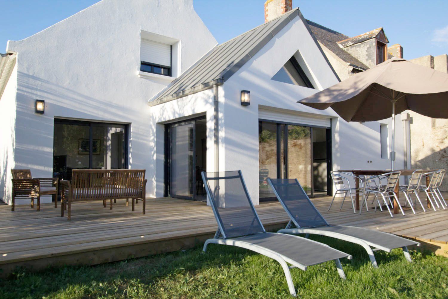 A modern house with a wooden deck, outdoor seating, and a large umbrella.