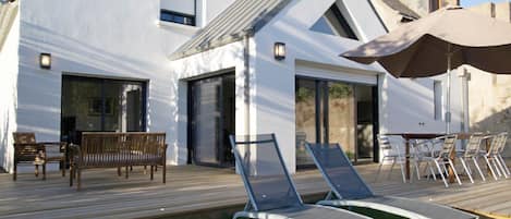 A modern house with a wooden deck, outdoor seating, and a large umbrella.