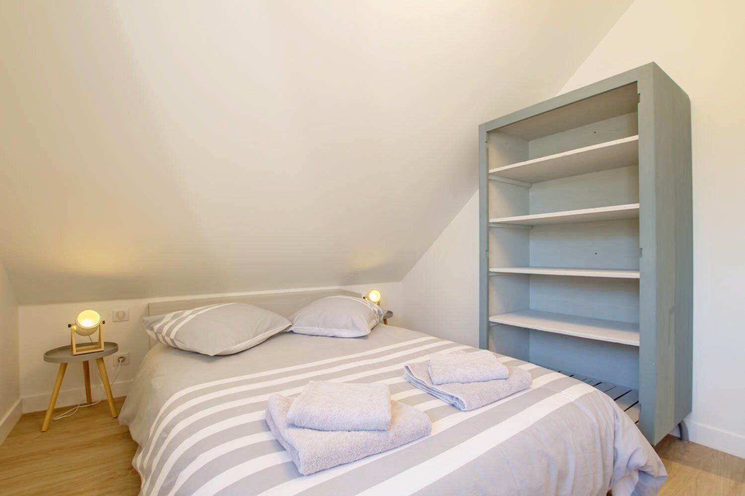 A bedroom with a bed, two bedside lamps, a striped bedspread, and a built-in shelving unit.