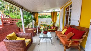 A covered patio area with wicker furniture, a glass coffee table, and a view of lush greenery. - Luxury karukera villa in st-francois with private pool tel0690071415 (saint-francois)