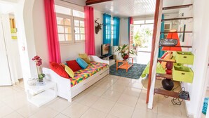 A bright living room with a white sofa, colorful cushions, a small table with a vase, and a bookshelf with various items. - Luxury karukera villa in st-francois with private pool tel0690071415 (saint-francois)