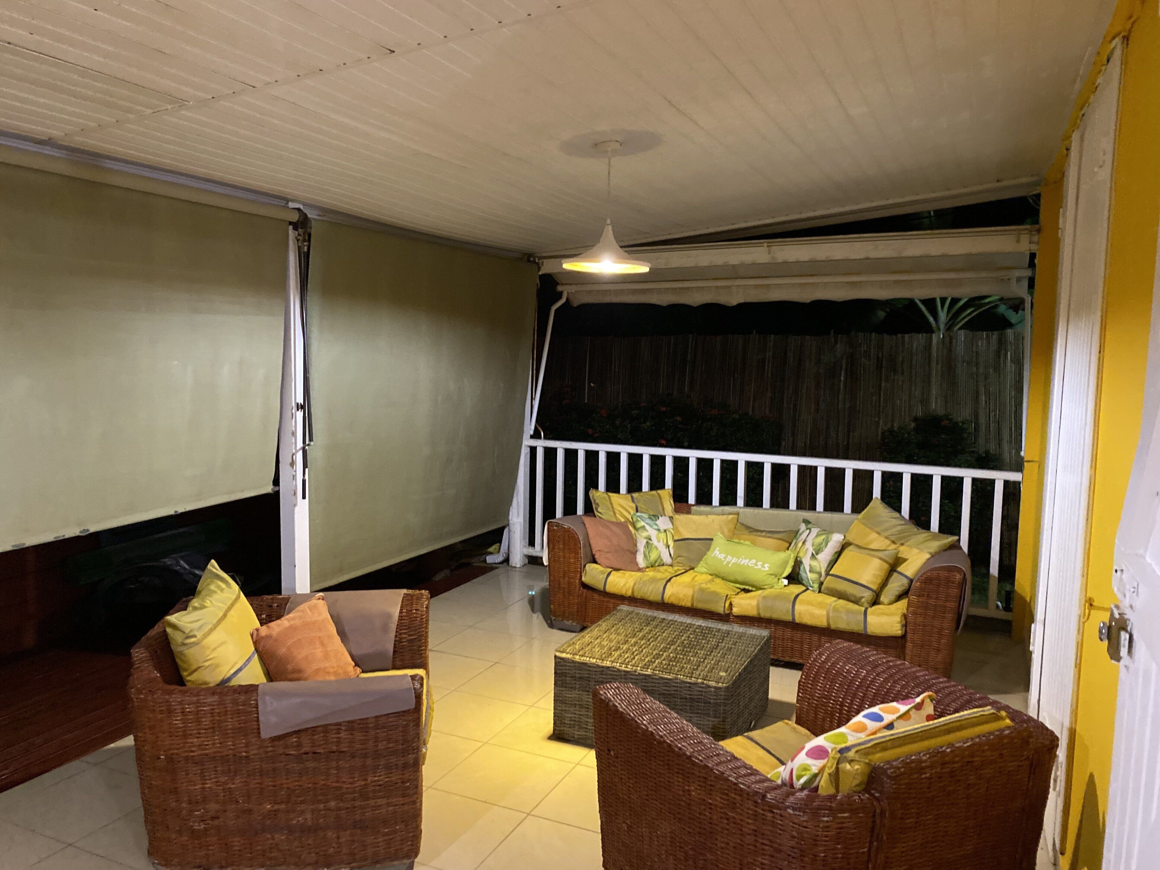 Un espace extérieur aménagé, abrité et doté de mobilier en osier, d’un canapé confortable, d’une petite table et d’une rambarde blanche.