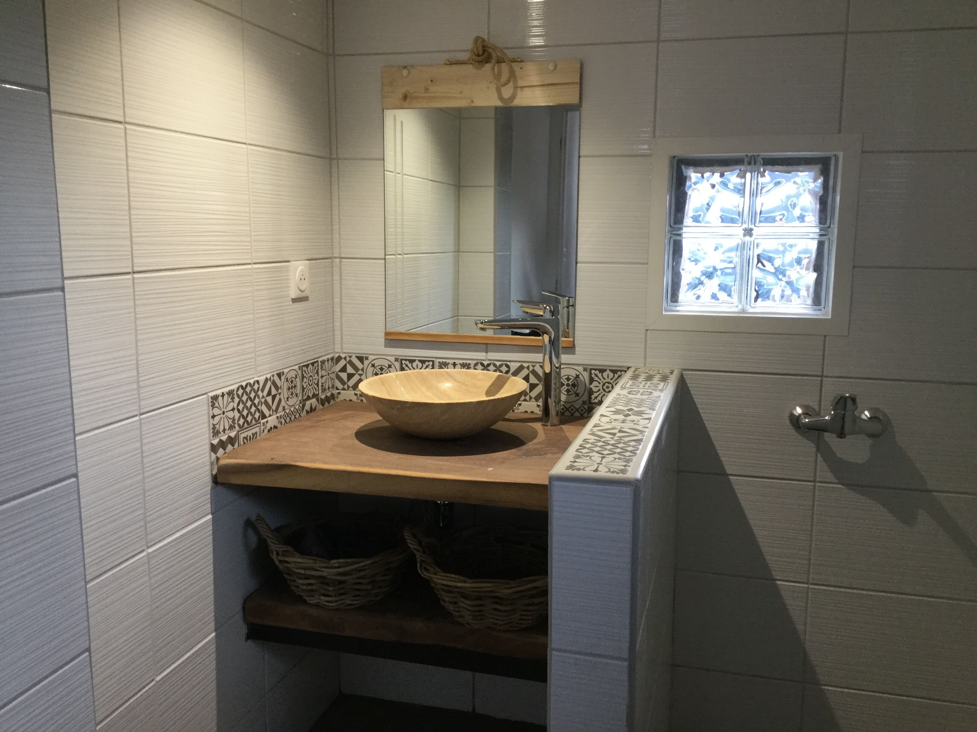 Un baño con un espejo grande, una encimera de madera y un lavabo tipo cuenco. Hay dos cestas debajo del lavabo y una ventana encima.