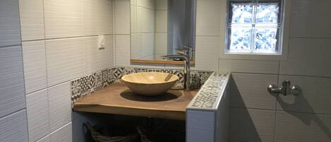 Un baño con un espejo grande, una encimera de madera y un lavabo tipo cuenco. Hay dos cestas debajo del lavabo y una ventana encima.