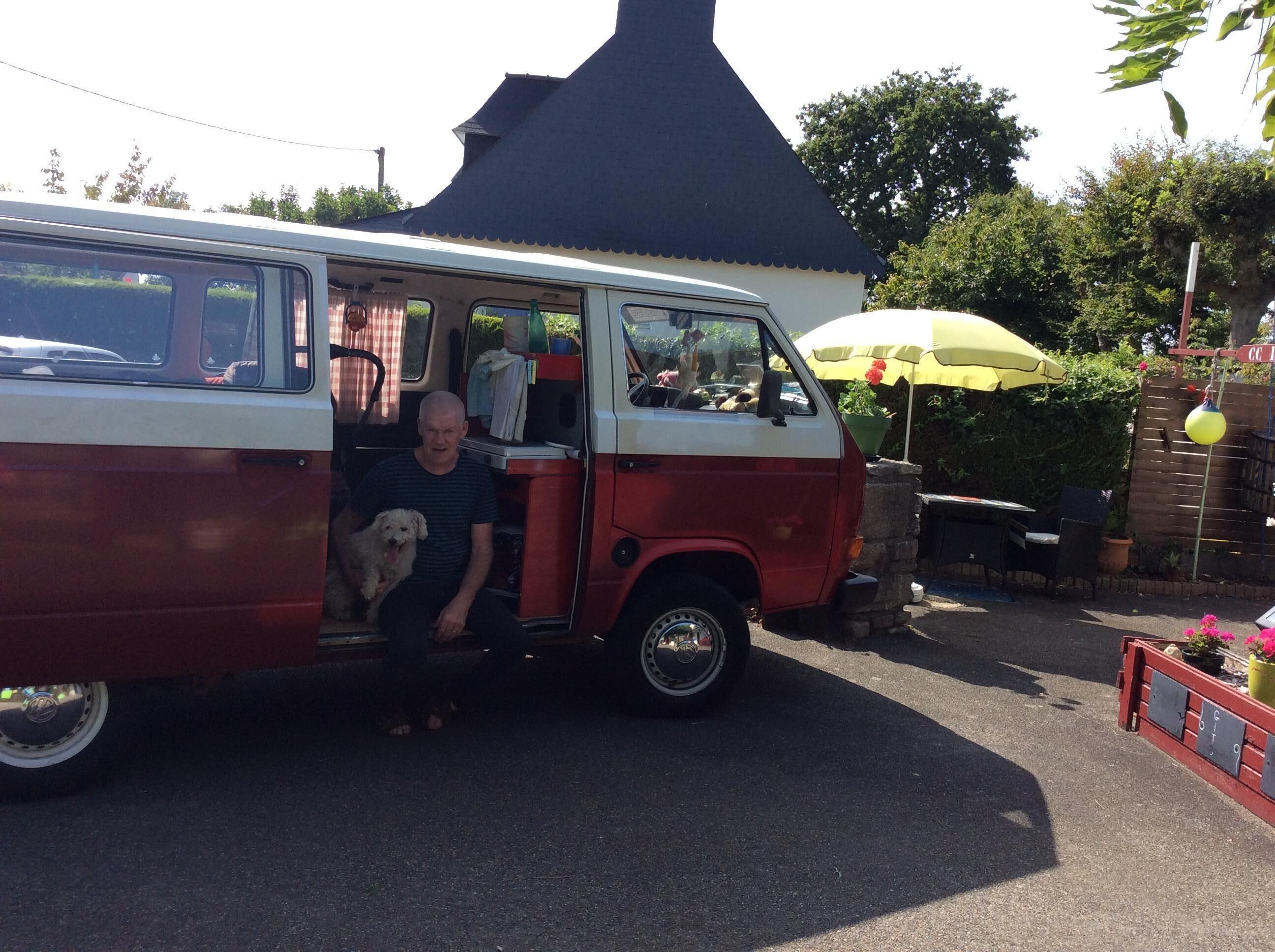 A red and white van parked in a driveway with a person and a dog inside.