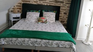 A bedroom with a stone wall, a bed with floral bedding, a nightstand, and a green curtain. - Relaxing holiday / wifi (Concarneau)
