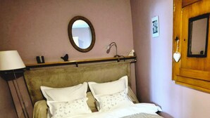 Een net opgemaakt bed met een gewatteerde spreidek, een bedlampje en een spiegel aan de muur.