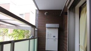 Un balcón estrecho con barandilla de vidrio, un refrigerador blanco pequeño y una puerta corrediza con cortina.