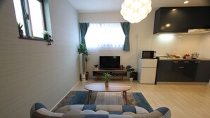 Una sala de estar moderna con un sofá, una mesa de centro, un televisor y una cocina con armarios y microondas.