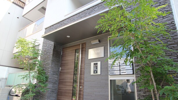 Un edificio moderno con fachada de piedra, un ventanal grande y una puerta con el rótulo "GIANZ".