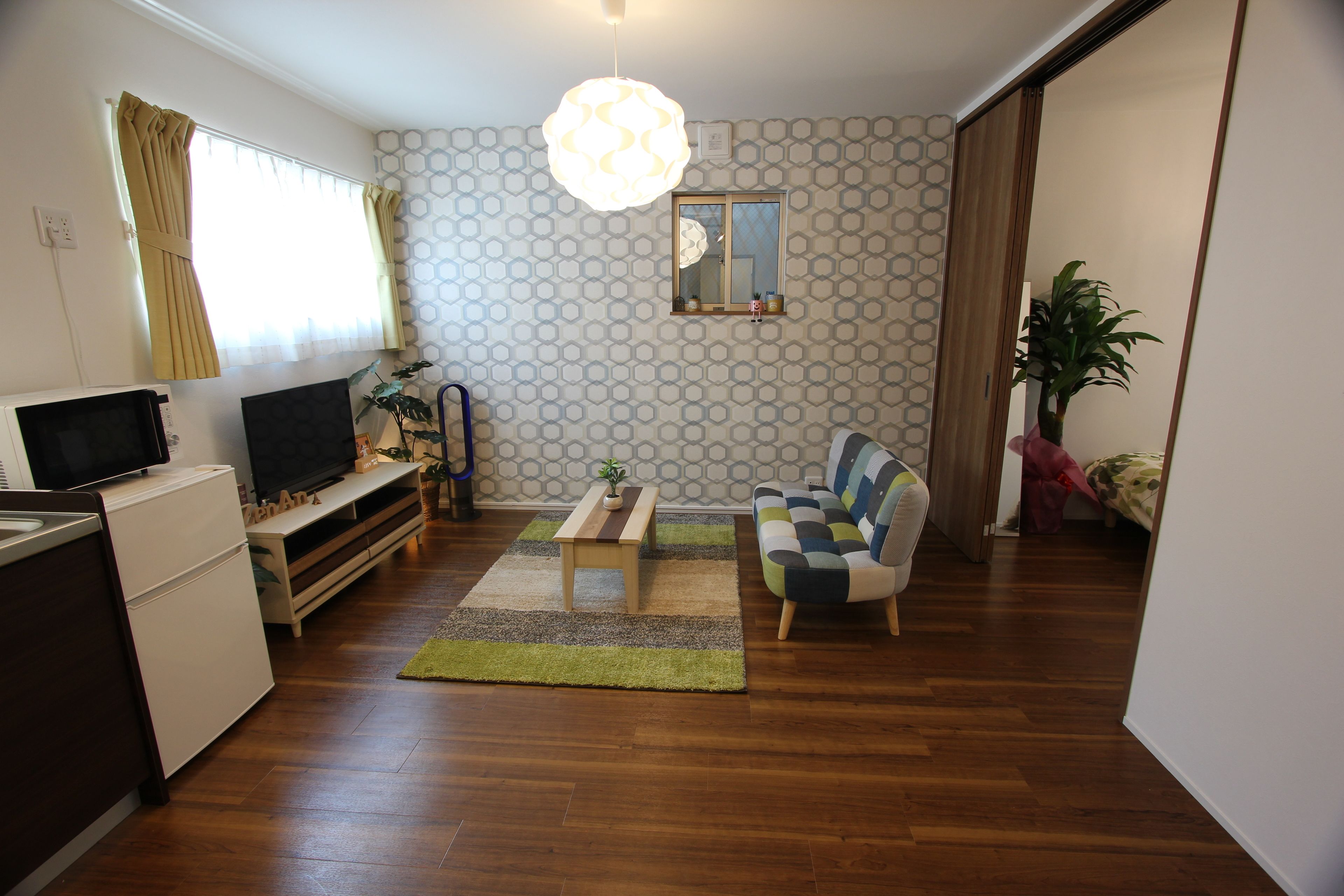 Un espace de vie compact avec un plancher en bois, un canapé, un téléviseur, une petite table et une plante en pot.
