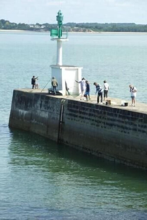 A concrete pier with a lighthouse structure, people standing and walking, and calm water. - Small seaside house, bright, very quiet, very large garden, Quimiac (Mesquer)