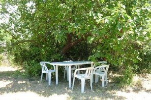 A round table with four white plastic chairs under a tree.