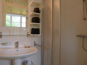 A bathroom with a white sink, a glass shelf with towels, and a shower area.