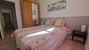 A bedroom with a bed, a bedside table, a nightstand, a door, and a wall with a painting. - The king of grau boucanet quiet apartment in villa entirely renovated (Le Grau-Du-Roi)