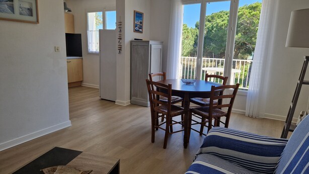 A dining area with a wooden table and chairs, a sofa, and a view of a balcony with trees. - The king of grau boucanet quiet apartment in villa entirely renovated (Le Grau-Du-Roi)