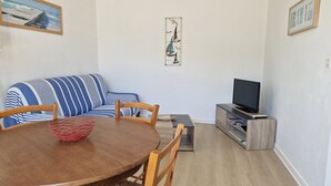 A living room with a blue-striped sofa, a wooden dining table with chairs, a TV on a wooden stand, and artwork on the walls. - The king of grau boucanet quiet apartment in villa entirely renovated (Le Grau-Du-Roi)