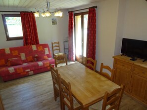 A cozy living room with a wooden dining table, red patterned sofa, and a television on a wooden cabinet.