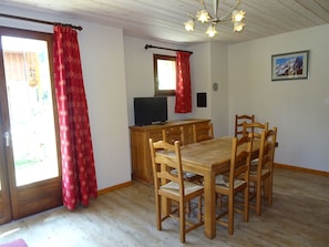 A dining area with a wooden table and chairs, a television on a wooden cabinet, and a chandelier.