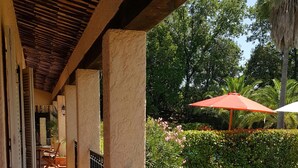 Een overdekt terras met een patio, een leuning en uitzicht op een tuin met een rode parasol.
