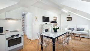 Una cocina moderna con armarios blancos, horno integrado y un comedor con mesa de mármol y sillas transparentes.